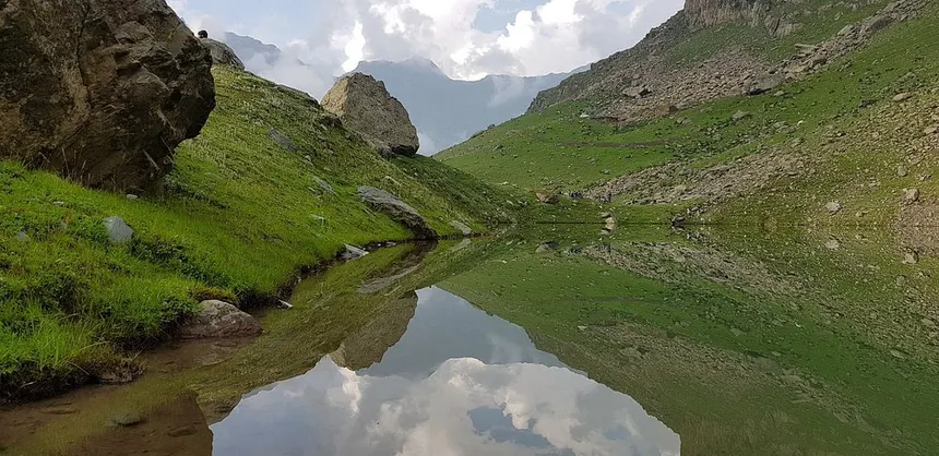 Mirror still alpine tarn reflecting clouds and rocky mountain slopes