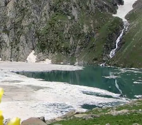 Partially frozen Thajiwas glacial tarn with snowmelt waterfall