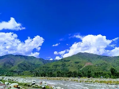 Suran River flowing under clear blue skies and green pine slopes
